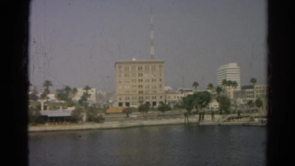 1966 Silver Lake, California home-movie frame showing a large shoreline building with an antenna beyond calm water and palms.