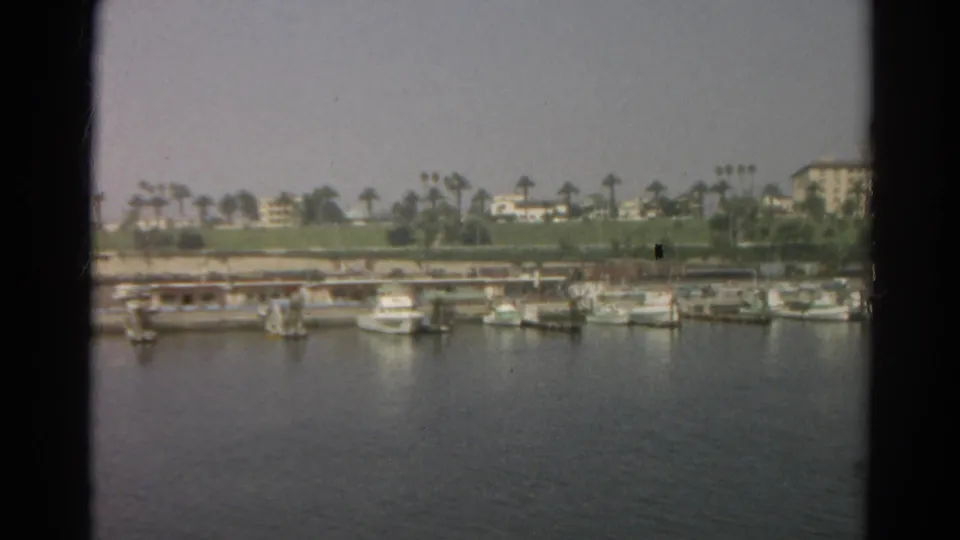 Soft 8mm frame of a Silver Lake waterfront marina with several docked boats, calm water, palms, and distant buildings.