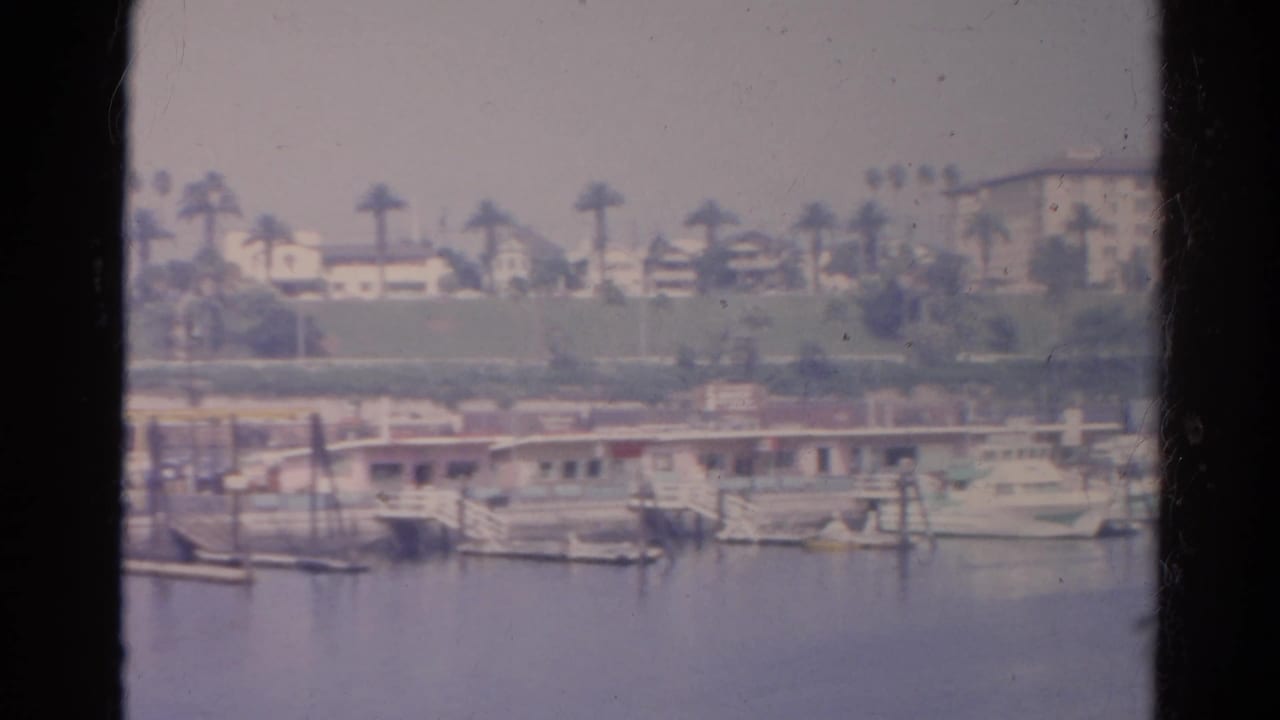 1966 Silver Lake view from a boat, with marina docks, moored boats, palms, and hillside residences across the water.