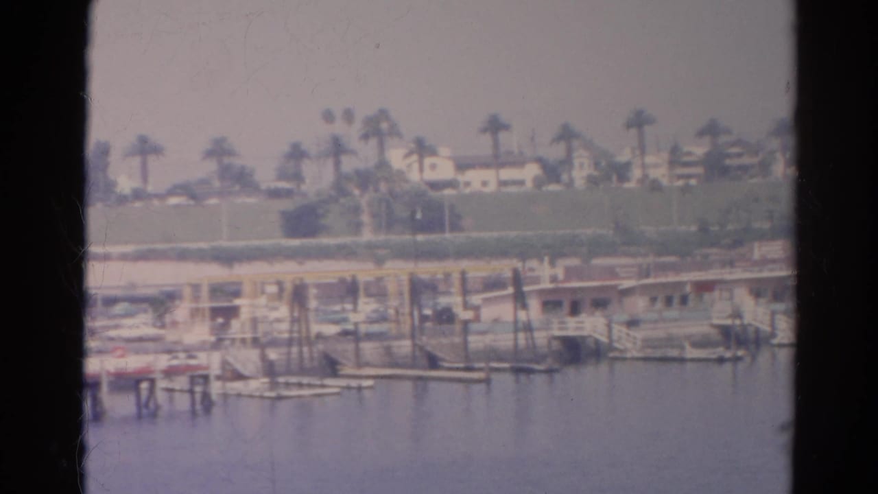 A soft 8mm frame of Silver Lake shoreline, showing dock posts, small boats, palms, and houses beyond the water.
