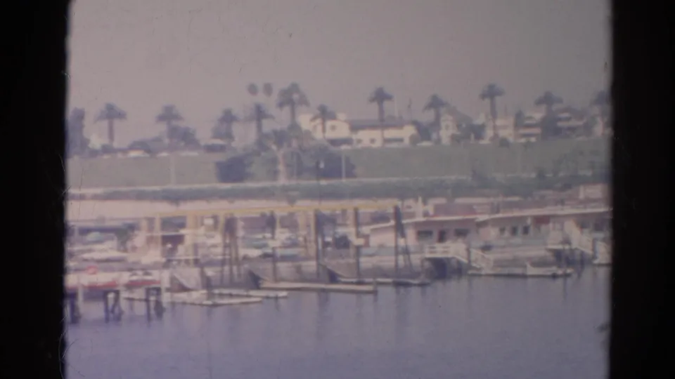 A soft 8mm frame of Silver Lake shoreline, showing dock posts, small boats, palms, and houses beyond the water.