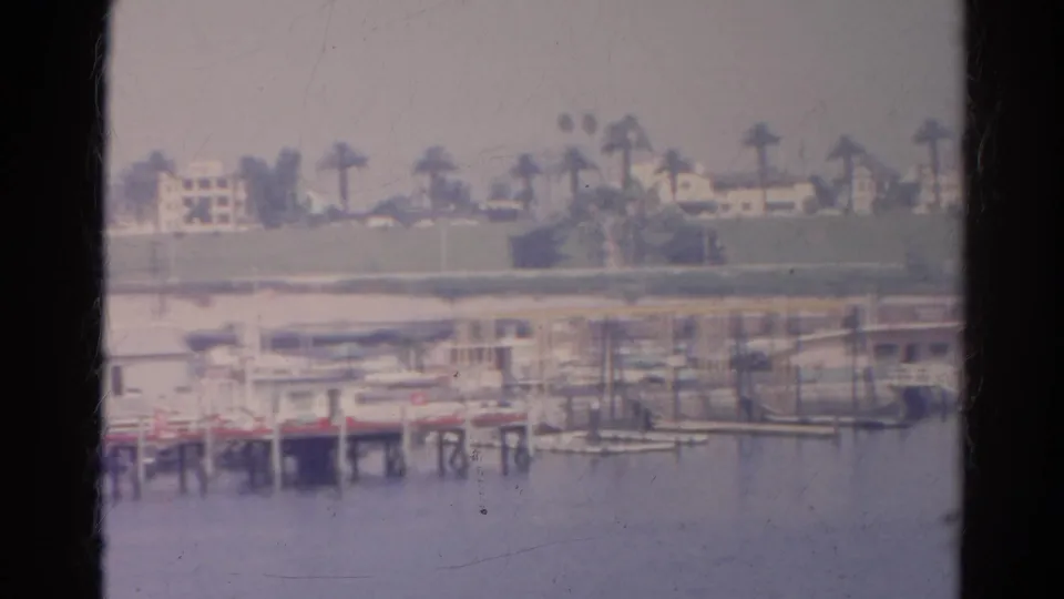 Silver Lake shoreline in 1966 with a low pier, small boats, palms, and hillside residences seen from a moving boat.