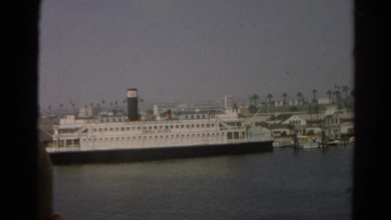 1966 8mm view of a white passenger ship docked across harbor water in the reported Silver Lake, California clip.