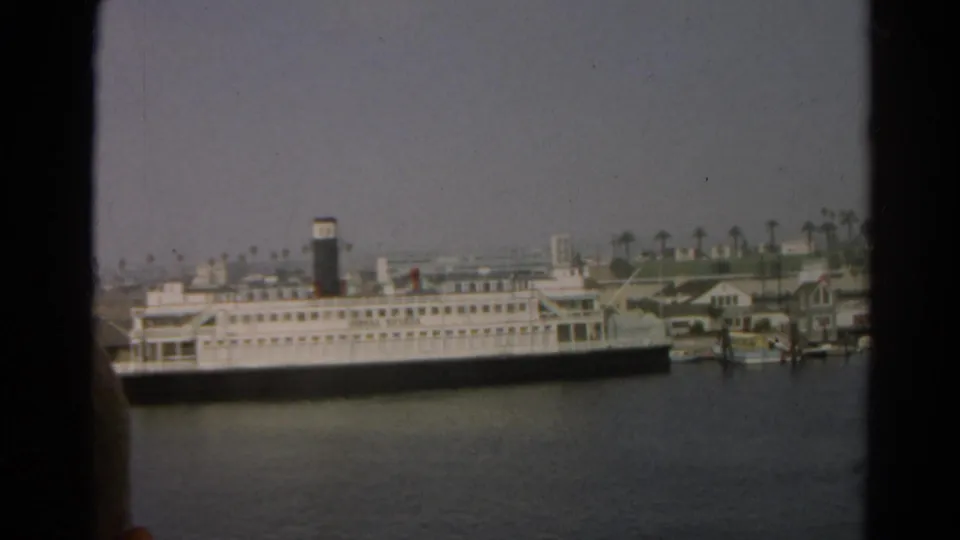 1966 8mm view of a white passenger ship docked across harbor water in the reported Silver Lake, California clip.