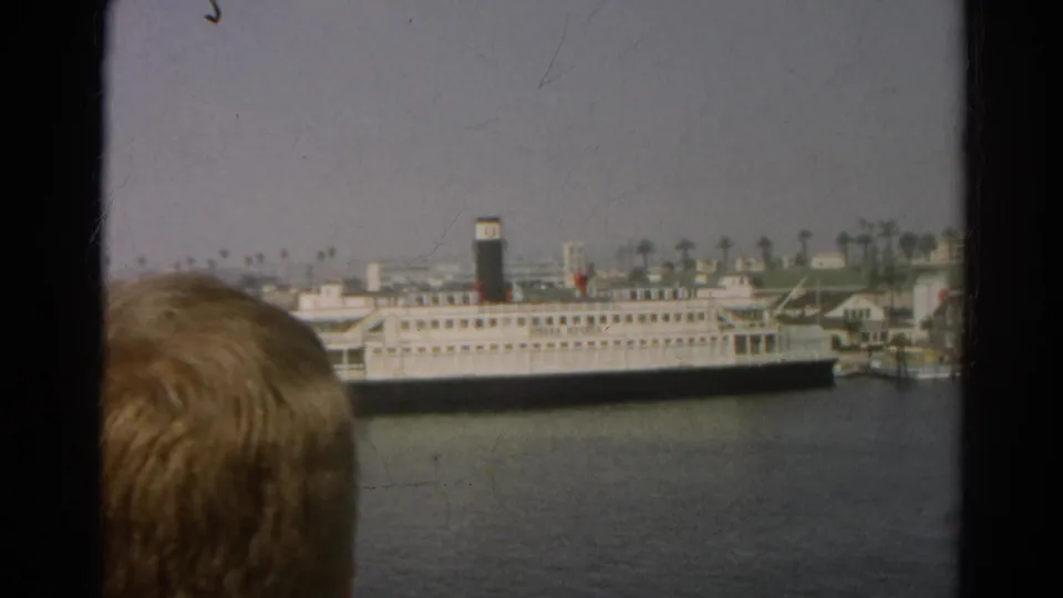 1966 8mm harbor view with a docked passenger ship and an incidental foreground head partly blocking the lower frame.