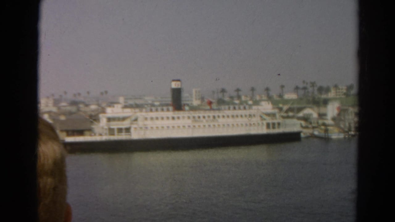 1966 California 8mm frame showing a large white passenger ship at a waterfront, with palm trees behind it and a partial viewer's head in the foreground.