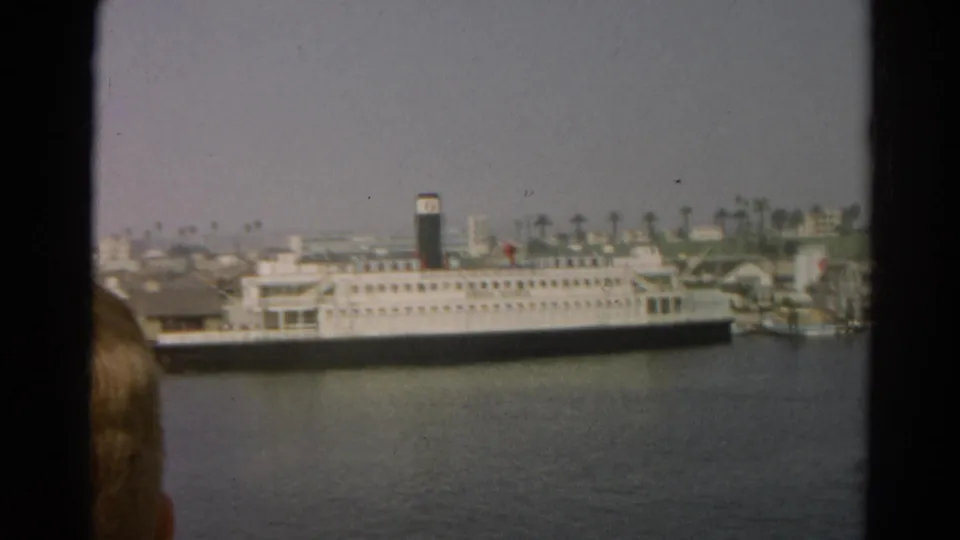 1966 California 8mm frame showing a large white passenger ship at a waterfront, with palm trees behind it and a partial viewer's head in the foreground.