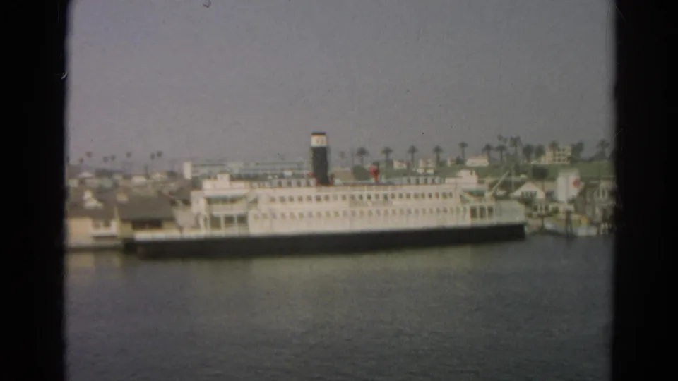 1966 California 8mm frame with a white multi-level passenger ship, dark hull band, black smokestack, and palm-lined shoreline in the background.