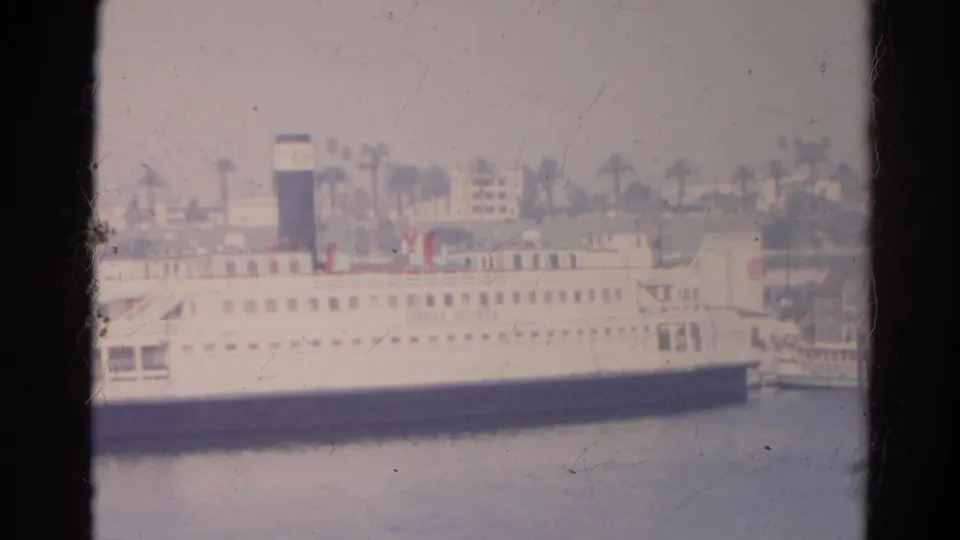 Overexposed 1966 California 8mm frame showing the white passenger ship closer in view, with deck windows, a black smokestack, and palm trees behind.