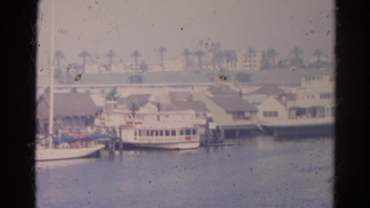 1966 home-movie frame showing small boats, dock structures, palms, and waterfront buildings in the listed California location.