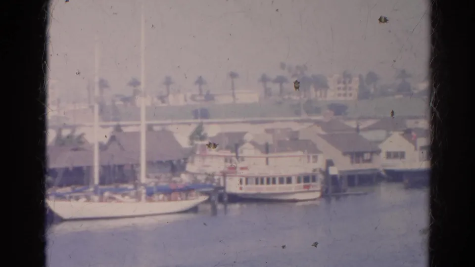 1966 8mm frame with a sailboat, docked passenger boat, low buildings, and palms along the listed Silver Lake waterfront.