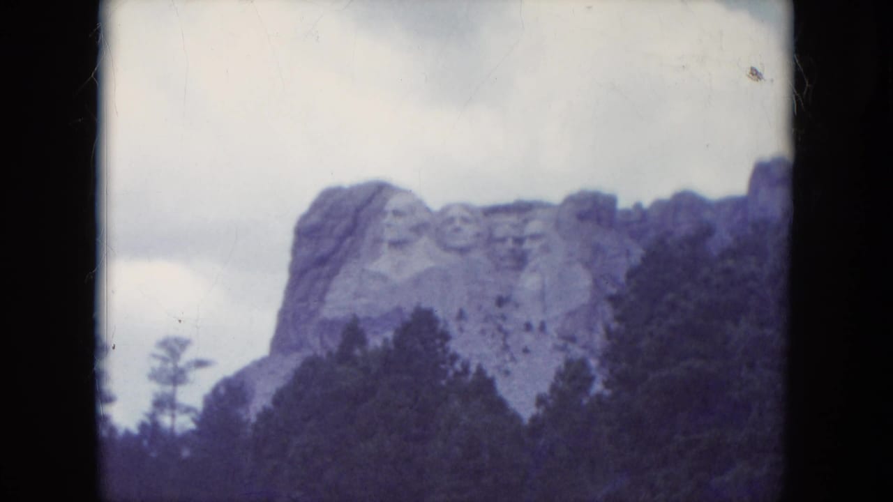 Mount Rushmore partly framed by trees under a cloudy sky.