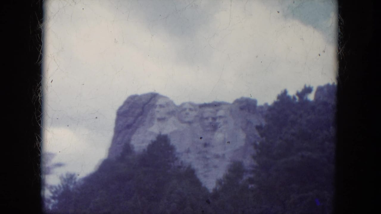 Distant view of Mount Rushmore above dark trees.