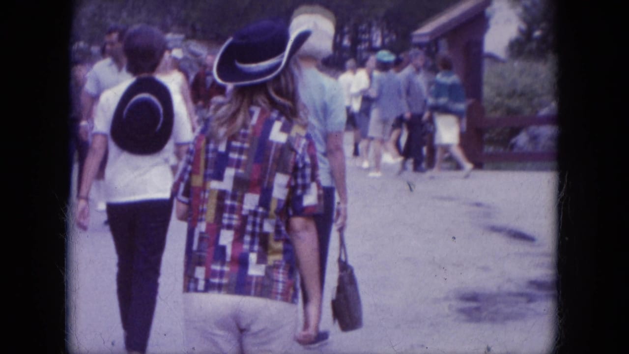 Tourists at Mount Rushmore walk away from the camera along a paved path, with period clothing and cowboy-style hats visible.