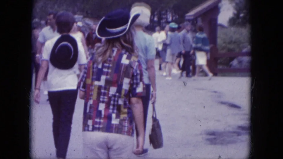 Tourists at Mount Rushmore walk away from the camera along a paved path, with period clothing and cowboy-style hats visible.
