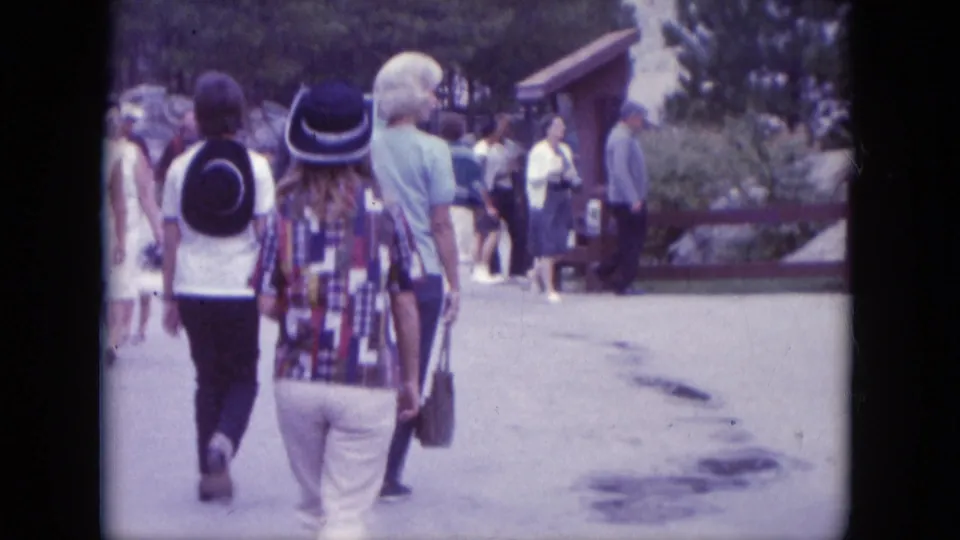 Visitor-shot 1966 footage follows tourists walking at Mount Rushmore, with a small building and trees along the path.