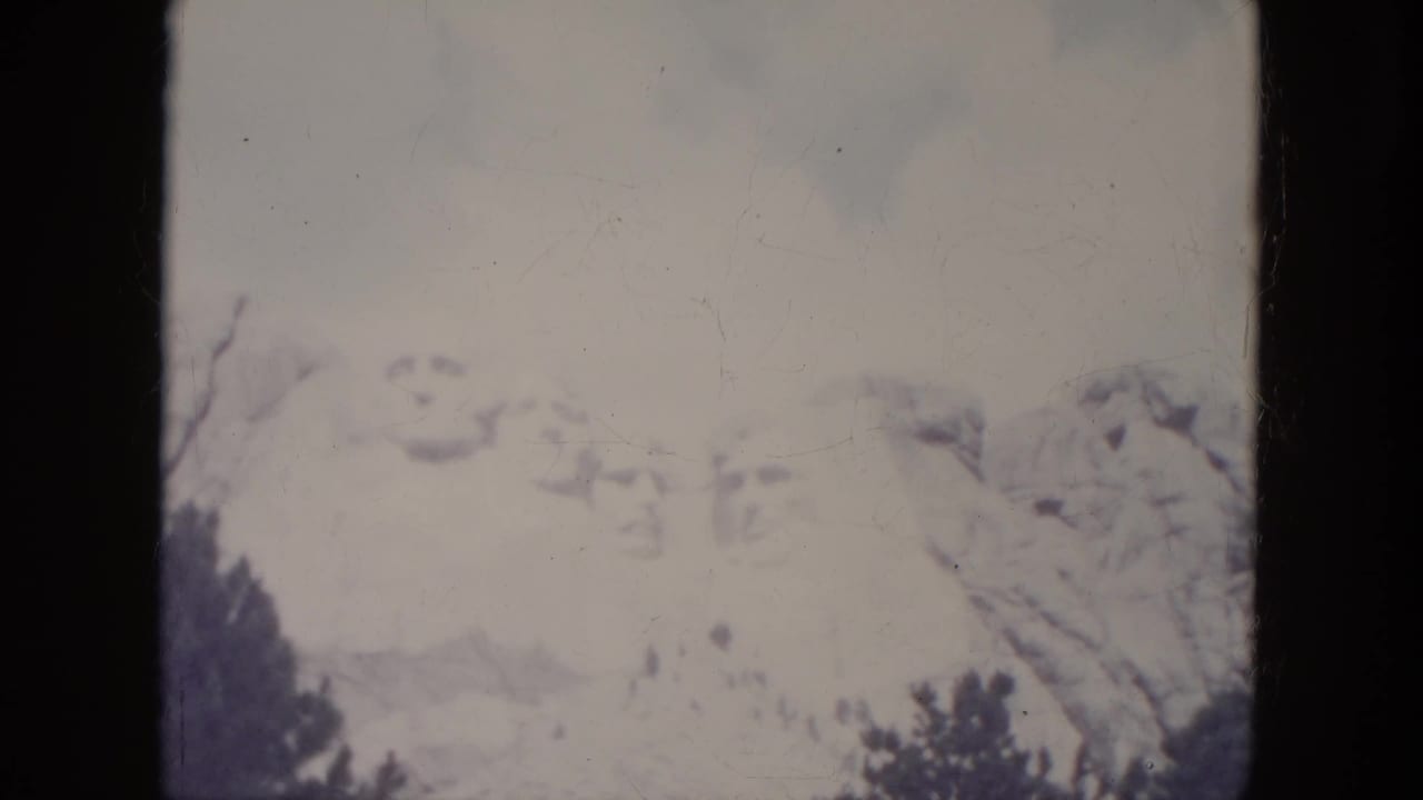 Soft view of Mount Rushmore with the carved faces faintly visible above dark trees.