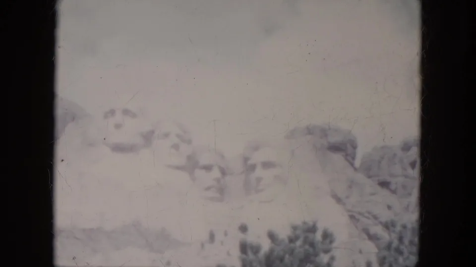 1966 8mm South Dakota frame holding on Mount Rushmore, with faint carved faces, trees, and aged film marks.
