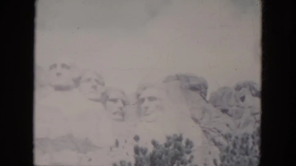 Faded 1966 8mm view of Mount Rushmore in South Dakota, with the carved presidential faces partly washed by exposure.