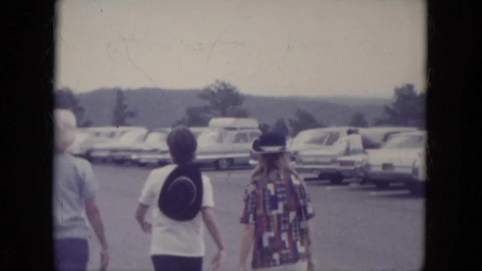 1966 South Dakota visitor scene with people seen from behind walking among parked mid-century cars near Mount Rushmore.