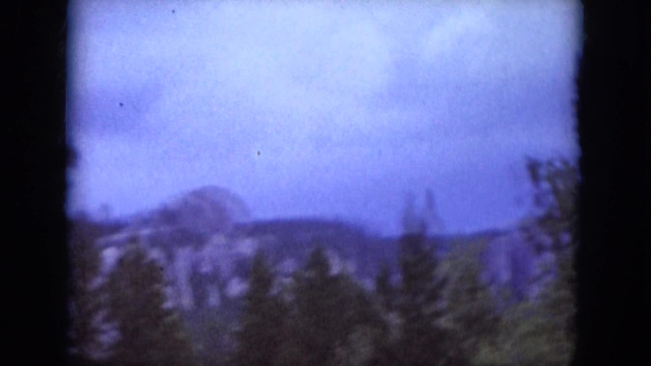 1966 South Dakota 8mm view of distant rock formations and wooded hills seen over pine trees.