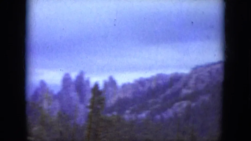 1966 South Dakota 8mm view of rugged rocks and evergreen trees, softened by haze and aged film color.