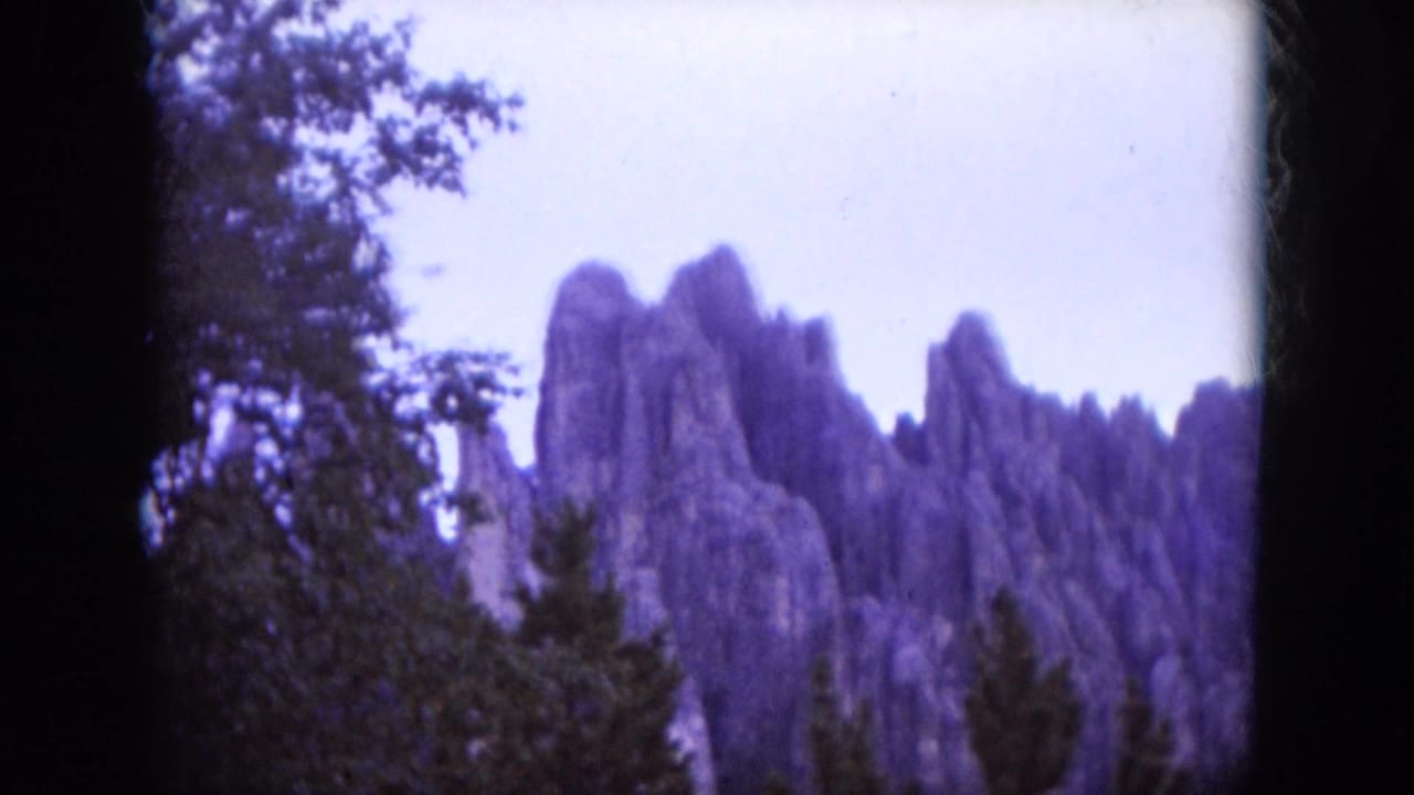 1966 South Dakota 8mm frame showing rocky formations partly framed by trees and heavy contact-sheet borders.