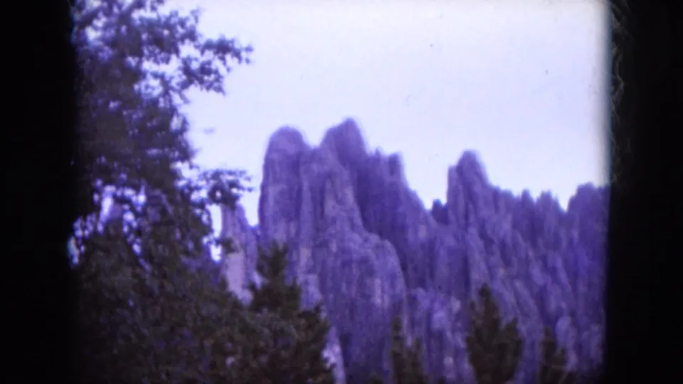 1966 South Dakota 8mm frame showing rocky formations partly framed by trees and heavy contact-sheet borders.