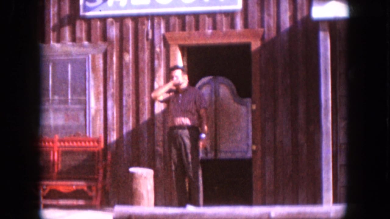 Man stands at a wooden saloon entrance beneath a painted sign.
