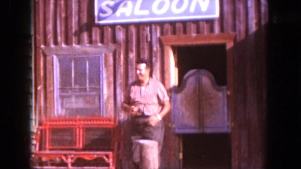 A man in a striped shirt walks past the window and red bench of a South Dakota saloon-themed storefront.