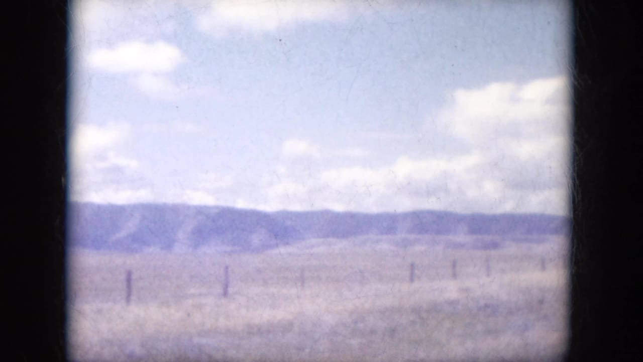 Rural South Dakota field with fence posts and distant low hills seen in faded 1960s 8mm color.