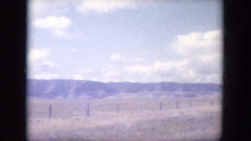 Rural South Dakota field with fence posts and distant low hills seen in faded 1960s 8mm color.
