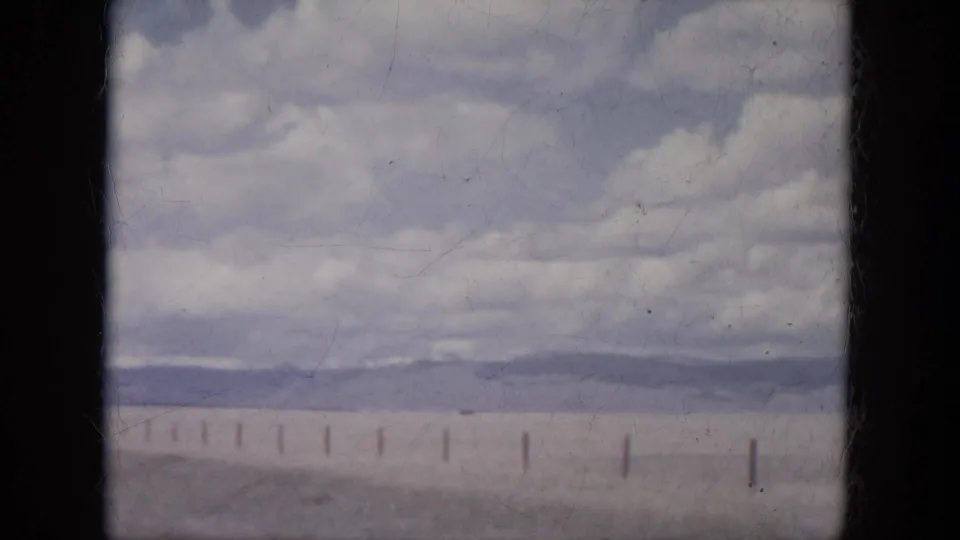 1966 South Dakota 8mm frame showing a roadside fence, open plains, distant hills, and soft clouds.