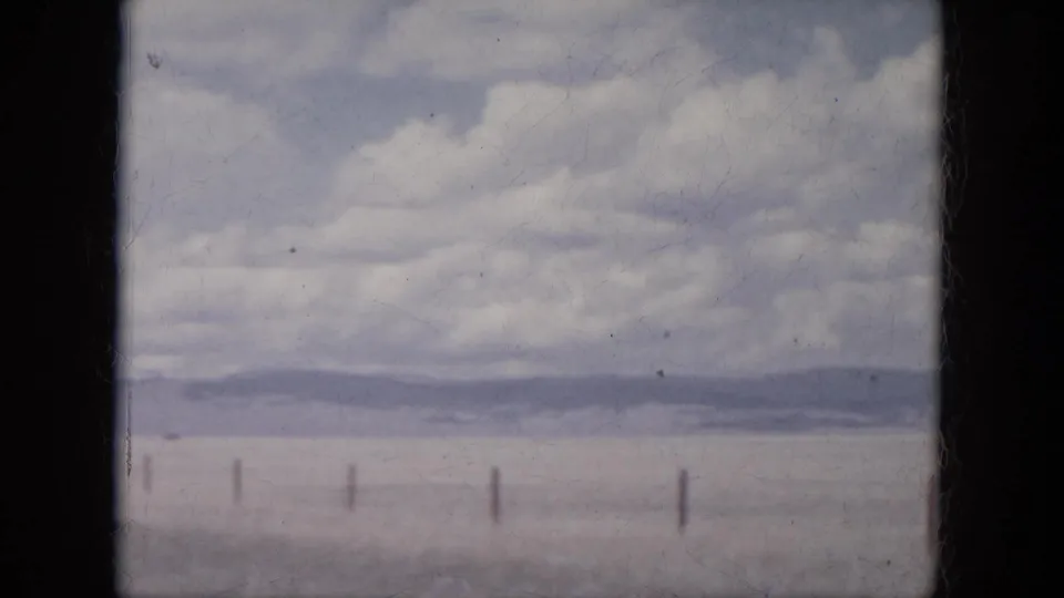 1966 South Dakota plains view with sparse fence posts, a hazy horizon, distant hills, and layered clouds.