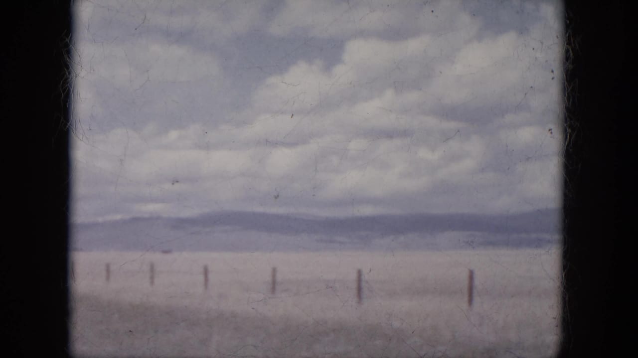 1966 South Dakota home-movie frame showing open plain, fence posts, distant hills, and a cloud-filled sky.
