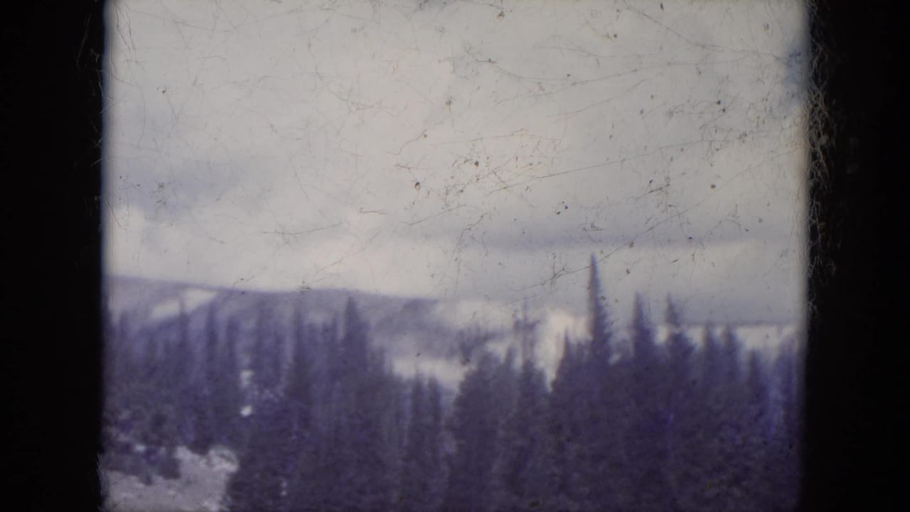 Evergreen-covered mountains and pale sky framed by dark film borders.
