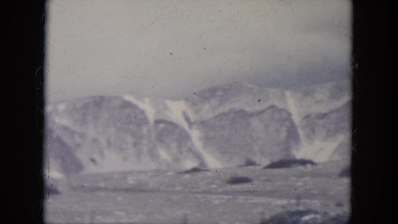 1966 South Dakota 8mm frame showing a soft, distant snowy mountain landscape with dark ground patches under a gray sky.