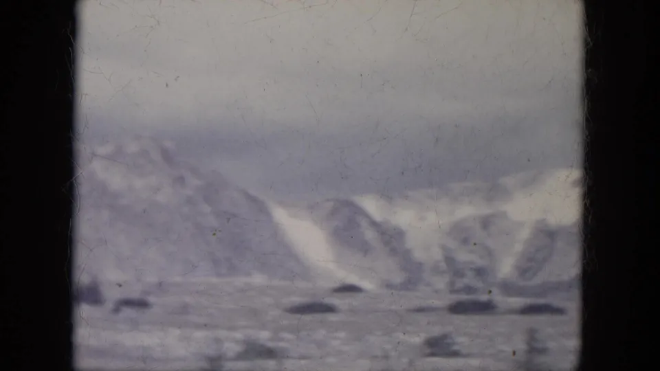 Soft 1966 South Dakota 8mm view of snowy hills and dark ground patches, with heavy grain and muted winter light.