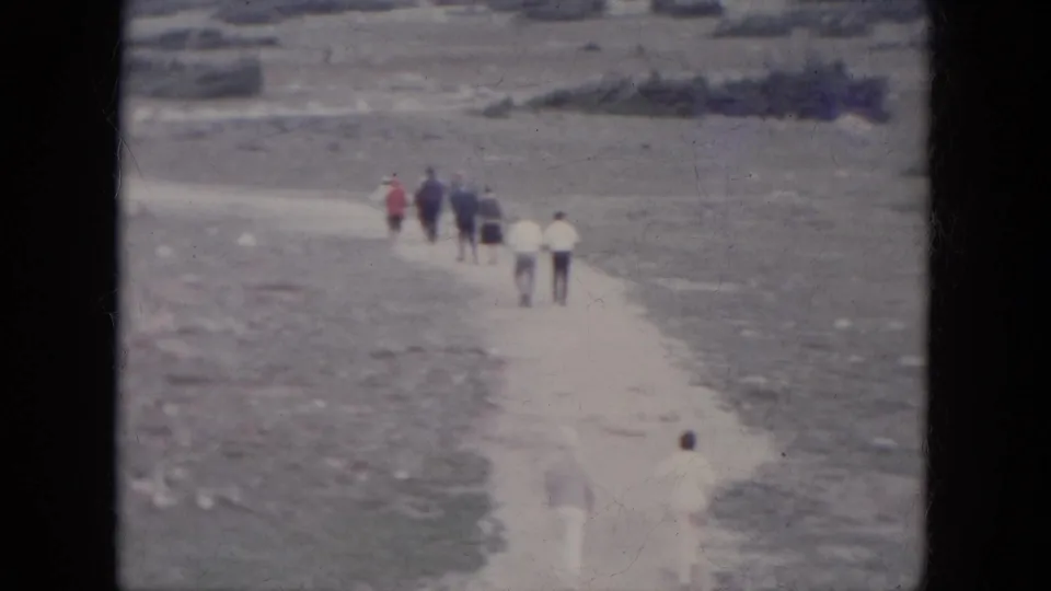 1966 South Dakota 8mm frame showing distant people walking in a line along a narrow pale path through winter terrain.