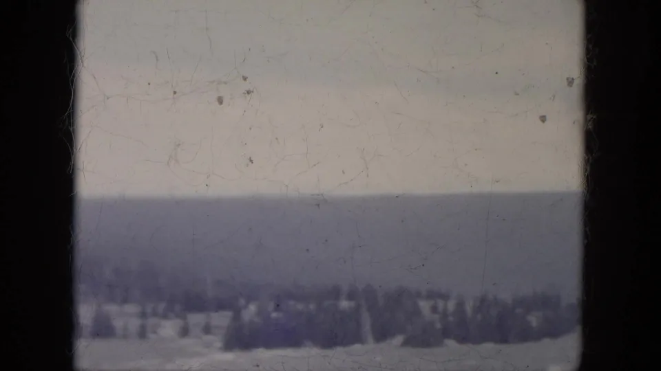 1966 South Dakota 8mm frame showing a distant evergreen line across snowy terrain under a pale winter sky.