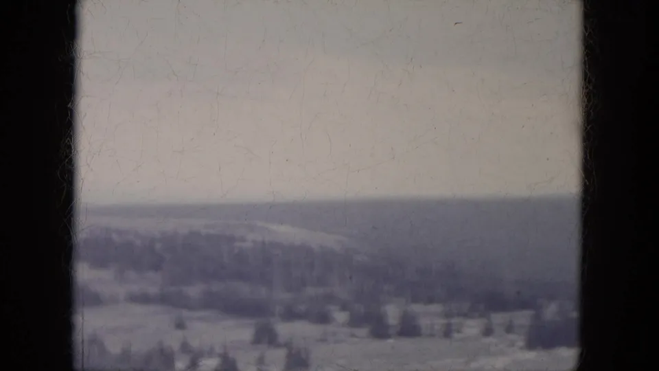 Vintage 8mm South Dakota landscape frame with snow-covered ground, scattered trees, and a hazy distant hill.