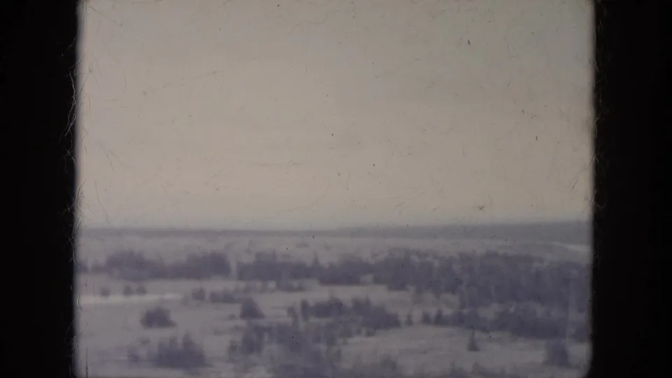 1966 South Dakota home-movie frame showing a wide winter hillside with scattered trees and muted 8mm color.