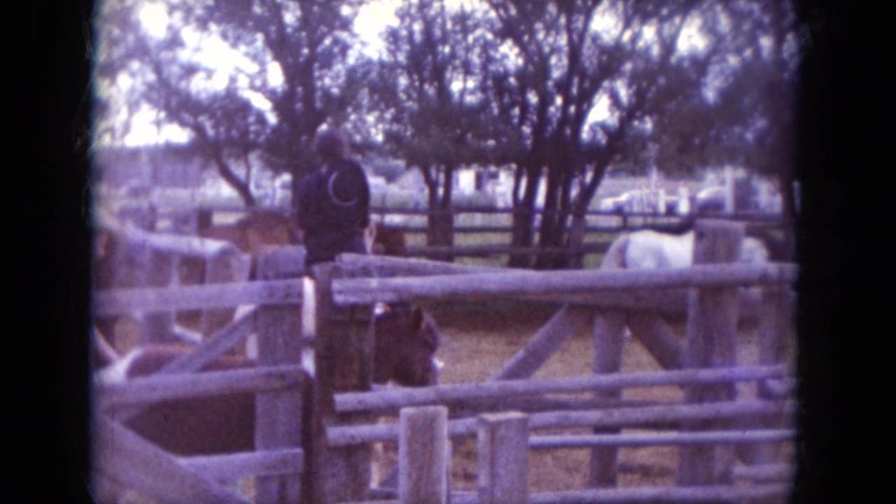 1966 South Dakota ranch scene with horses, riders, trees, and wooden corral fencing in a home-movie frame.