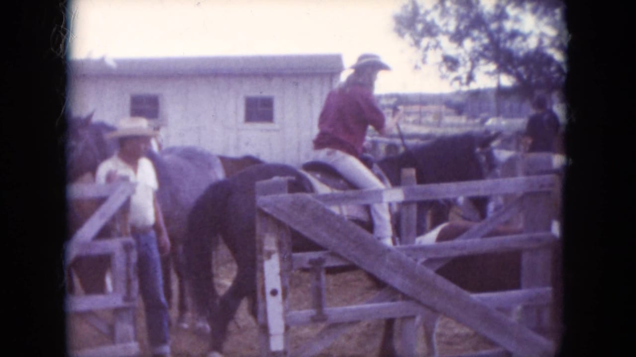 1966 South Dakota 8mm frame showing a red-shirted rider on horseback beside a wooden corral, with another person in a cowboy hat nearby.