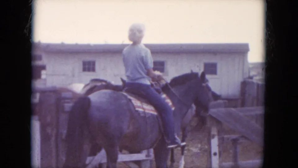 1966 South Dakota 8mm frame showing a rear view of a rider on horseback moving through a wooden corral area with a pale barn behind.