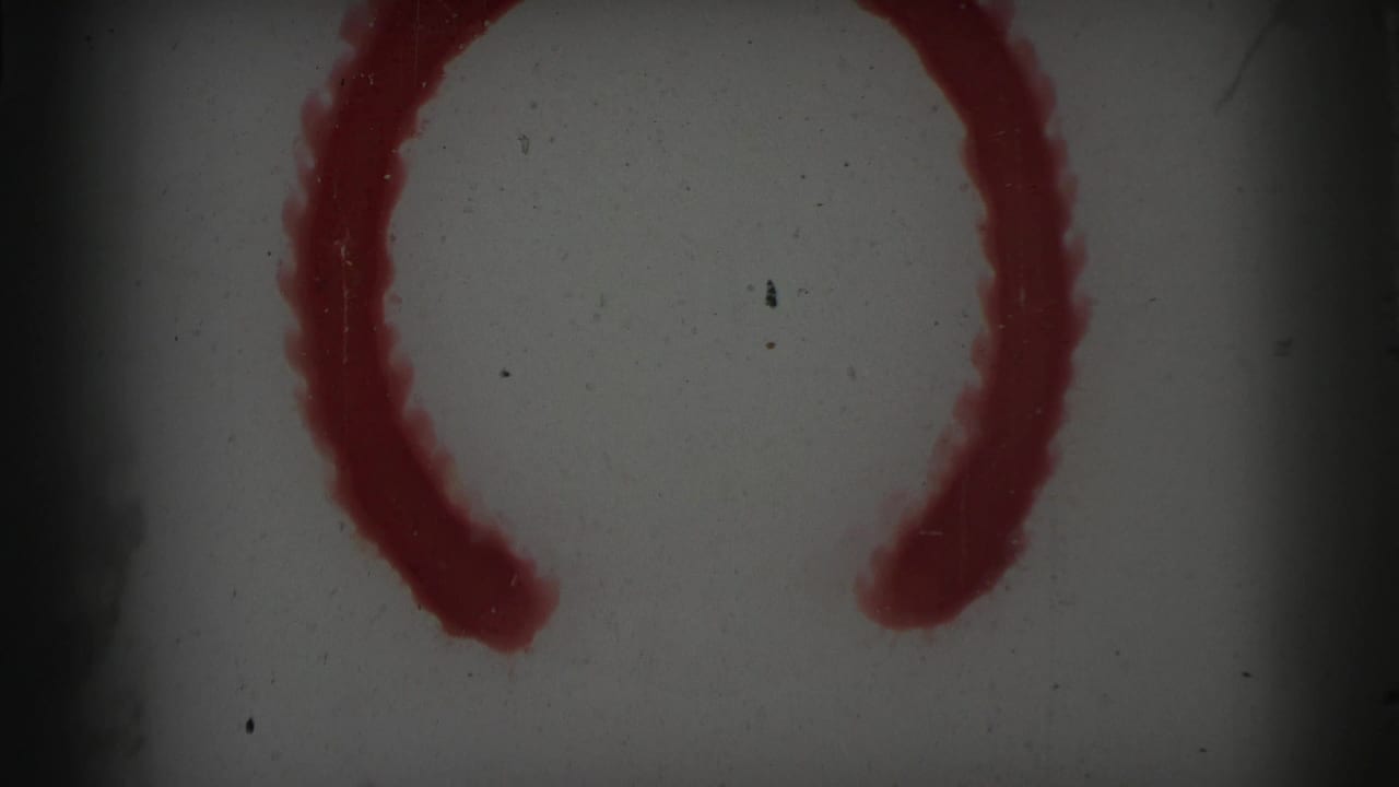 Gray film frame with a red curved painted mark and heavy speckling.