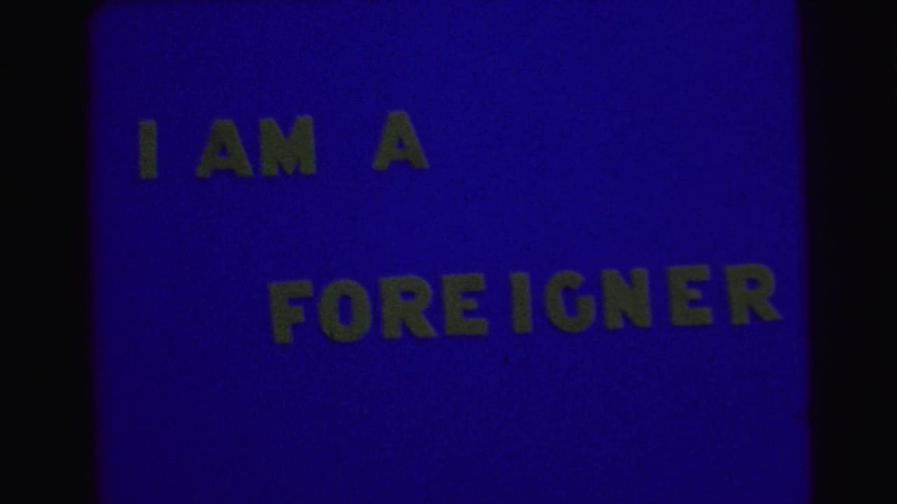 Blue film frame with yellow block text reading I AM A FOREIGNER.