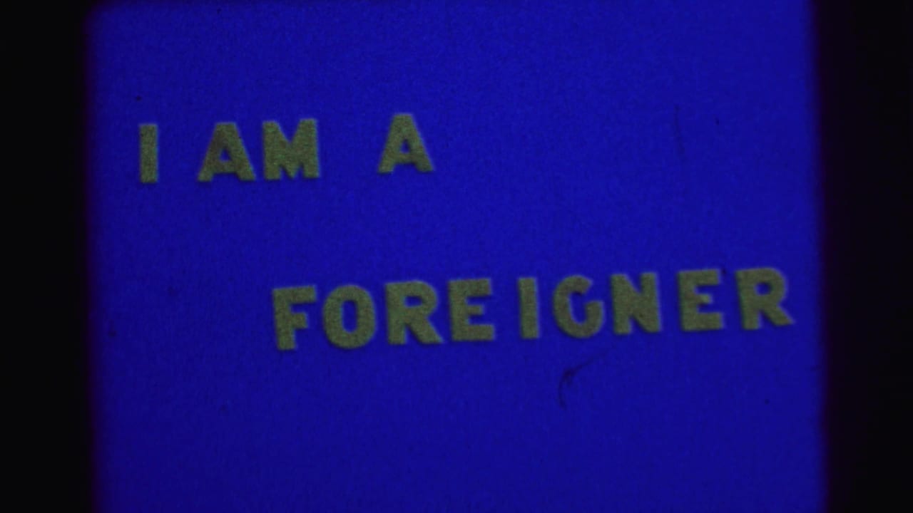 Blue title card with yellow text reading I AM A FOREIGNER and dark film edges.