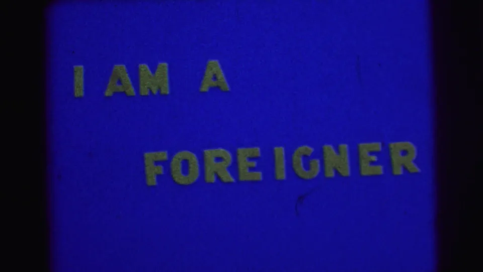 Static 1967 Brazil 8mm title card showing yellow I AM A FOREIGNER lettering against a blue background.