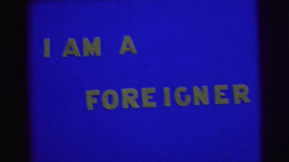 1967 Brazil home-movie title card with yellow block letters reading I AM A FOREIGNER on a blue background.